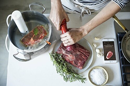 Person seasoning steak with herbs, sous vide cooking in progress.